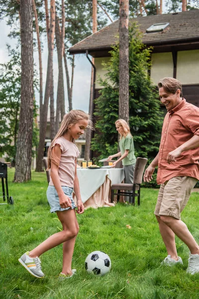 Smiling kid playing football with father near mother and table outdoors — Stock Photo