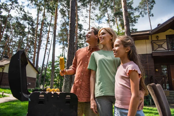 Familia sonriente parada cerca de la parrilla durante el fin de semana - foto de stock