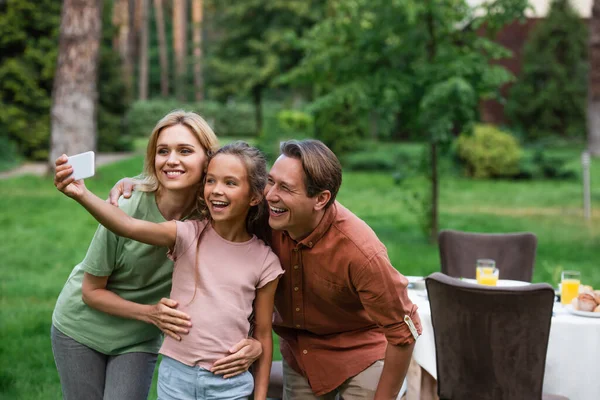 Cheerful kid taking selfie with parents near table outdoors — Stock Photo