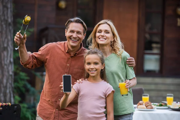 Smiling kid showing smartphone near parents with food and orange juice outdoors — Stock Photo