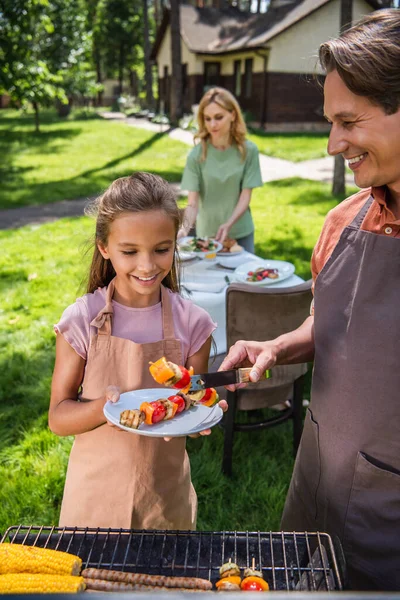 Sorrindo pai segurando legumes grelhados perto da filha com placa ao ar livre — Fotografia de Stock