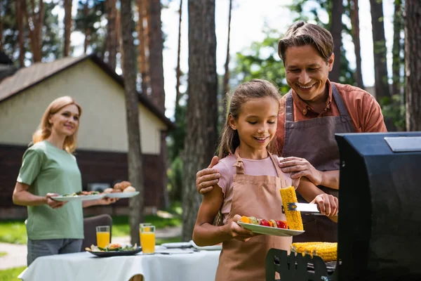 Lächelnder Vater steht neben Tochter mit Mais und Gemüse beim Picknick — Stockfoto