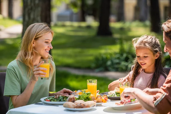 Donna che tiene succo d'arancia vicino alla famiglia e cibo durante il picnic — Foto stock