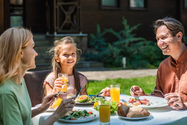 Famille positive avec de la nourriture et du jus d'orange parlant pendant le pique-nique — Photo de stock