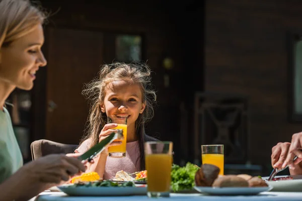 Усміхнена дитина тримає апельсиновий сік біля батьків і їжі на відкритому повітрі — стокове фото