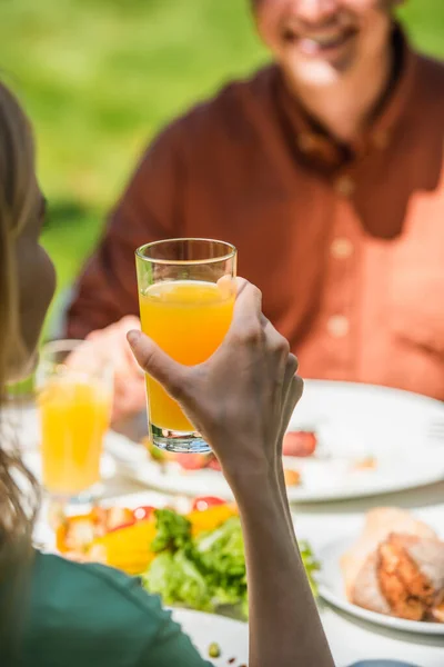 Mulher desfocada segurando suco de laranja perto de comida e marido ao ar livre — Fotografia de Stock