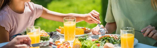 Vista recortada del niño sosteniendo tenedor cerca de la ensalada y los padres al aire libre, pancarta - foto de stock