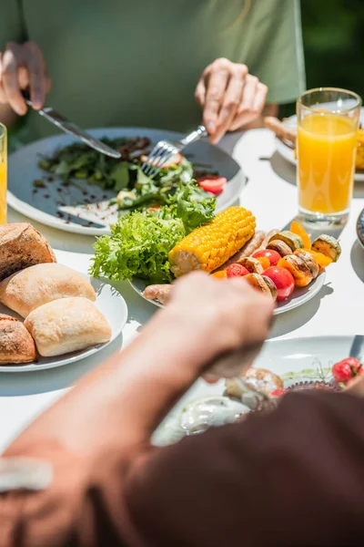 Vista recortada de verduras a la parrilla cerca de la pareja borrosa al aire libre - foto de stock