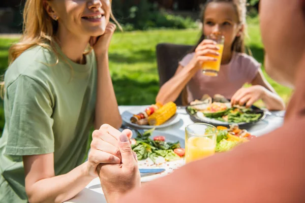 Padres tomados de la mano cerca de la comida y niños borrosos al aire libre - foto de stock