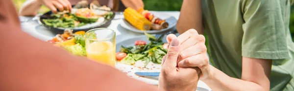 Cropped view of parents holding hands near kid and blurred food outdoors, banner — Stock Photo