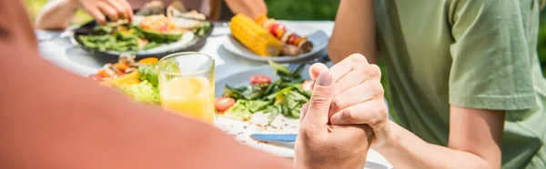 Обрізаний вид батьків, що тримають руки біля дитини і розмиті продукти харчування на відкритому повітрі, банер — стокове фото