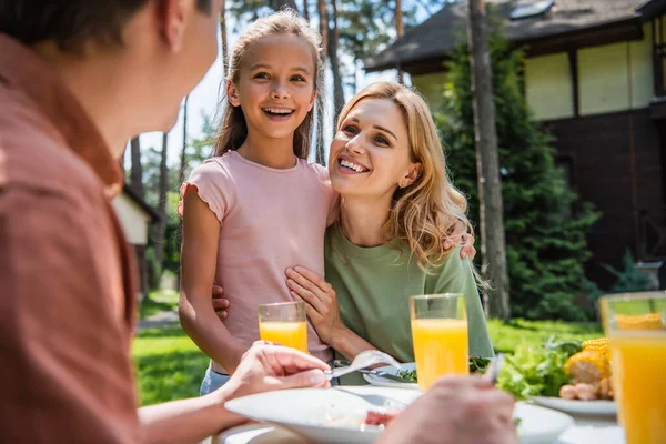 Mujer positiva y niño mirando a padre borroso durante el picnic - foto de stock