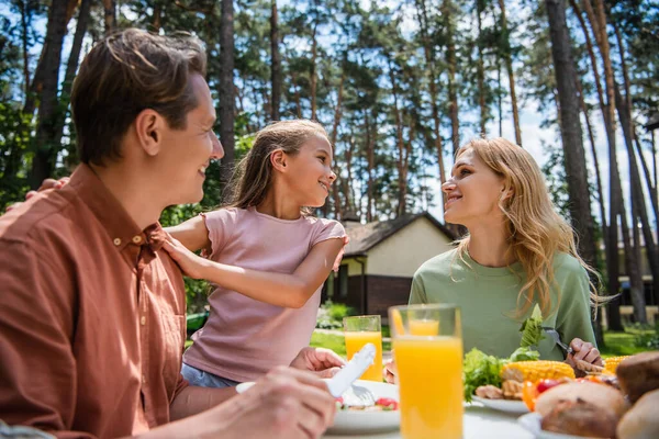 Seitenansicht des lächelnden Kindes umarmt Vater in der Nähe der Mutter und leckeres Essen im Freien — Stockfoto