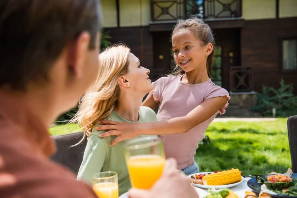 Lächelndes Kind umarmt Mutter beim Picknick neben verschwommenem Vater im Freien — Stockfoto