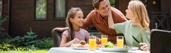 Mujer positiva tocando marido cerca de niño y comida al aire libre, bandera - foto de stock