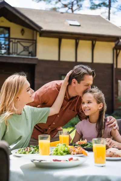 Homme embrasser fille souriante près de la femme et de la nourriture à l'extérieur — Photo de stock