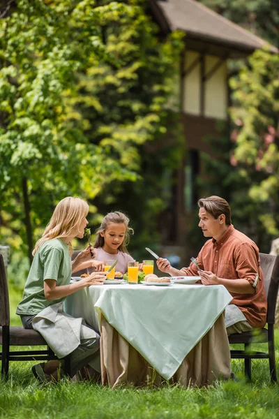 Famiglia mangiare cibo gustoso vicino succo d'arancia all'aperto durante il fine settimana — Foto stock