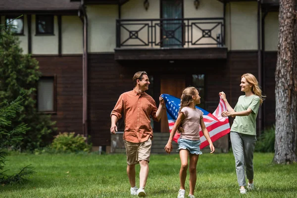 Des parents positifs tenant un drapeau américain près d'un enfant à l'extérieur — Photo de stock