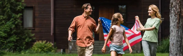 Genitori sorridenti che tengono la bandiera americana vicino alla figlia all'aperto, banner — Foto stock