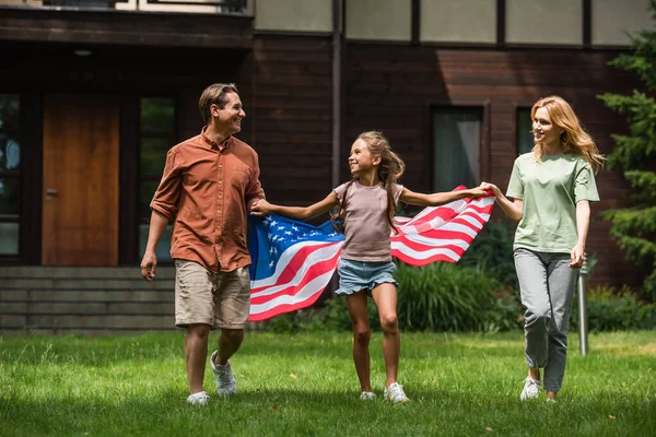Enfant avec drapeau américain tenant la main des parents sur la pelouse — Photo de stock