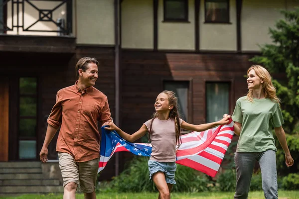 Souriante fille tenant drapeau américain et les mains de parent à l'extérieur — Photo de stock