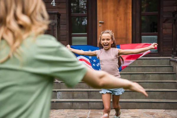 Enfant excité avec le drapeau américain courant à la mère floue à l'extérieur — Photo de stock