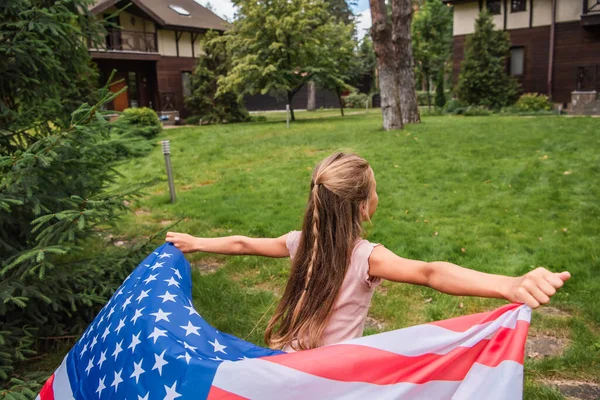 Niño preescolar con bandera americana corriendo en el césped - foto de stock