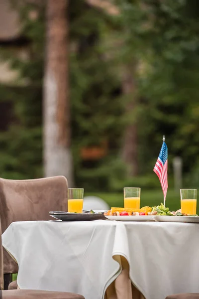 Bandera americana cerca de comida y jugo de naranja en la mesa al aire libre - foto de stock