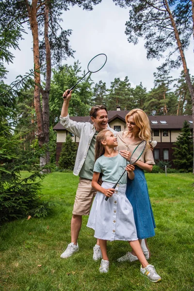 Familia sonriente con raquetas de bádminton abrazándose en el césped - foto de stock