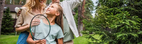 Enfant souriant avec raquette de badminton regardant les parents à l'extérieur, bannière — Photo de stock