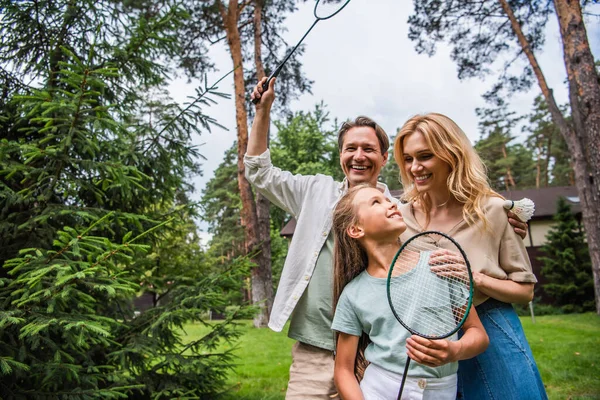 Família positiva com raquetes de badminton abraçando ao ar livre — Fotografia de Stock