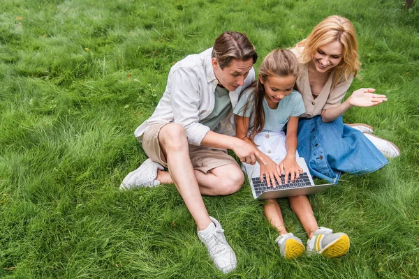 Високий кут зору усміхненої сім'ї з ноутбуком на траві — стокове фото