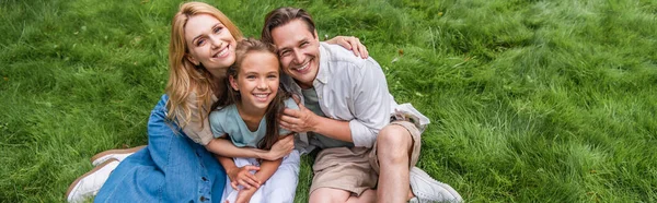 Vue grand angle des parents embrassant un enfant souriant sur l'herbe, bannière — Photo de stock