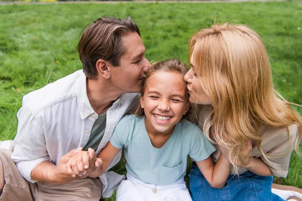 Родители целуют дочь на лужайке — стоковое фото