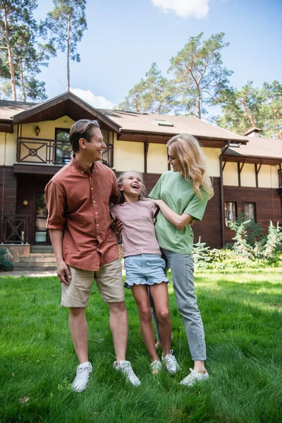 Parents hugging excited daughter on grass outdoors — Stock Photo