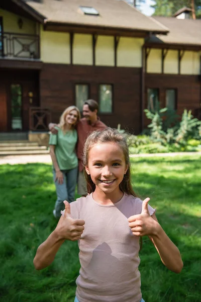 Smiling child showing like near blurred parents outdoors — Stock Photo