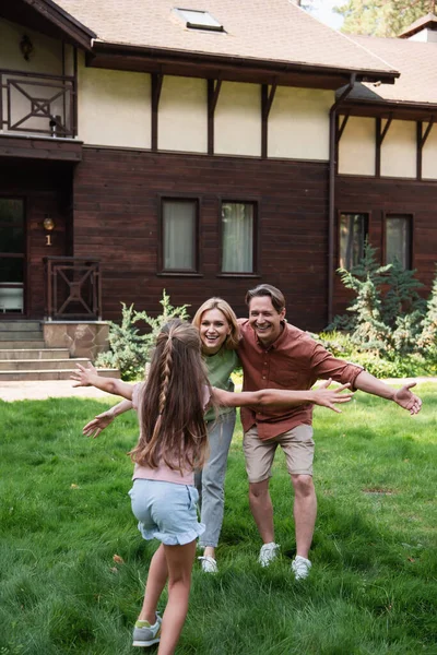 Menina correndo para pais sorridentes perto de casa de férias — Fotografia de Stock