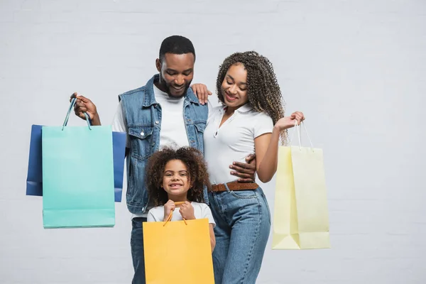 Família afro-americana feliz segurando sacos de compras multicoloridos em cinza — Fotografia de Stock