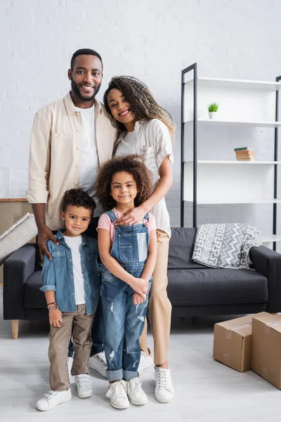 Heureux couple afro-américain avec des enfants regardant la caméra tout en se tenant dans un nouvel appartement — Photo de stock