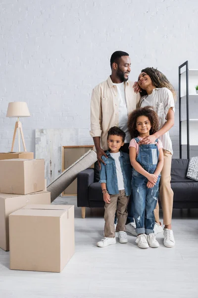Щаслива афроамериканська сім'я посміхається біля картонних коробок в новій квартирі — стокове фото