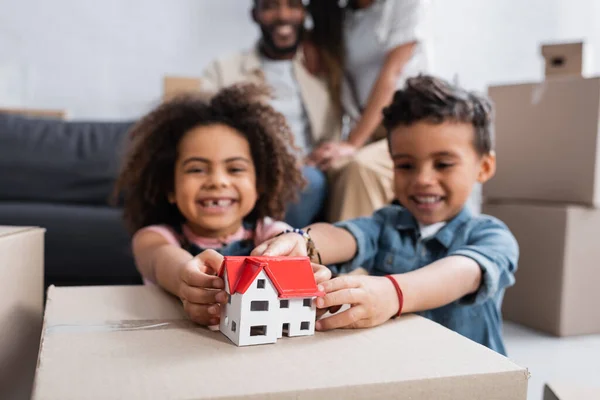 Crianças americanas africanas alegres perto do modelo da casa e pais no fundo borrado — Fotografia de Stock