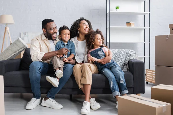 Heureuse famille afro-américaine regardant loin tout en étant assis sur le canapé dans un nouvel appartement — Photo de stock