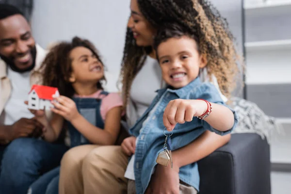 Selective focus of key in hand of african american boy sitting near blurred family — Stock Photo