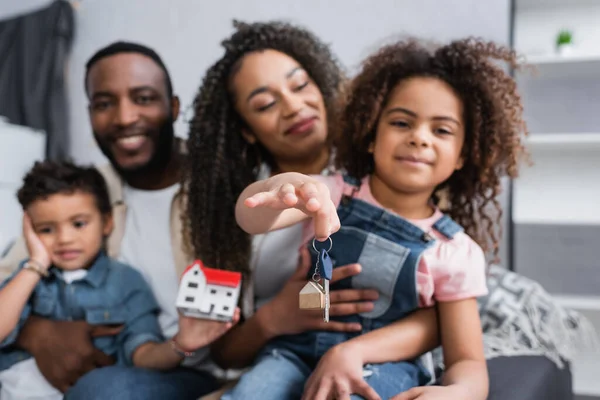 Selective focus of key in hand of cheerful african american girl near blurred family — Stock Photo