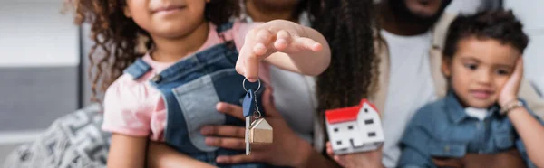 Vista parcial de la chica afroamericana sosteniendo llave cerca de la familia borrosa, pancarta - foto de stock