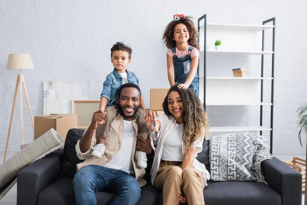 Happy african american woman showing key near family in new apartment — Stock Photo