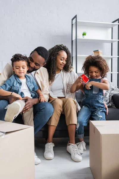 Familia afroamericana sentada en sofá cerca de cajas de cartón - foto de stock