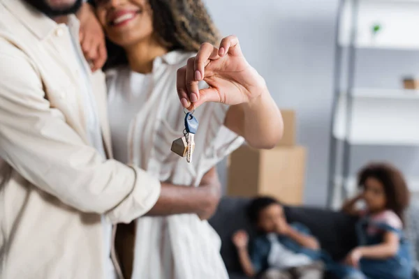 Sonriente afroamericana mujer sosteniendo la llave de nuevo apartamento cerca de marido y borrosa niños - foto de stock