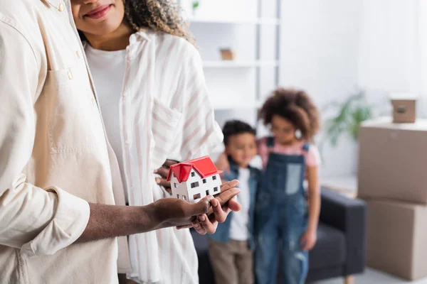 African american couple standing with house model near kids on blurred background — Stock Photo