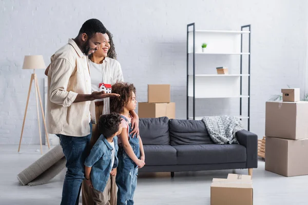 Afro-américaine holding maison modèle près de la famille heureuse dans le nouvel appartement — Photo de stock